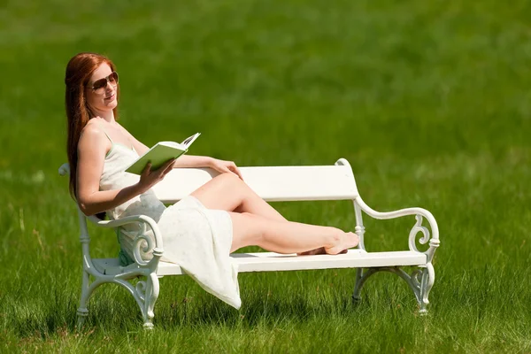 红头发女人读本书坐在草地上 白色长椅上浅景深 — 图库照片