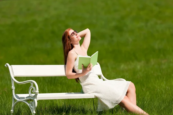 Mujer pelirroja relajándose en el banco blanco en primavera —  Fotos de Stock