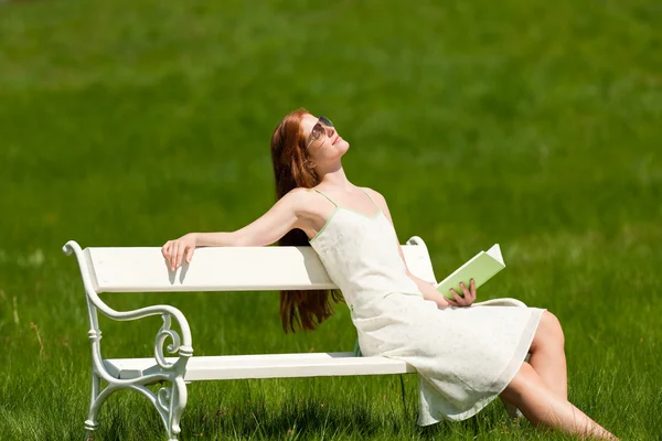 红头发女人放松着本书坐在草地上 白色长椅上浅景深 — 图库照片