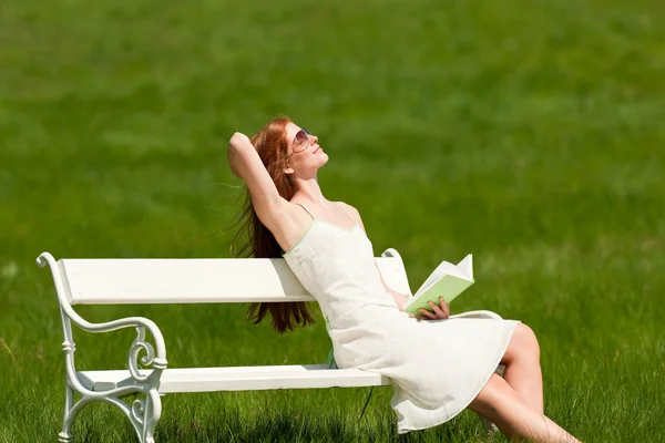 Рыжая женщина наслаждается солнцем на белой скамейке весной — стоковое фото