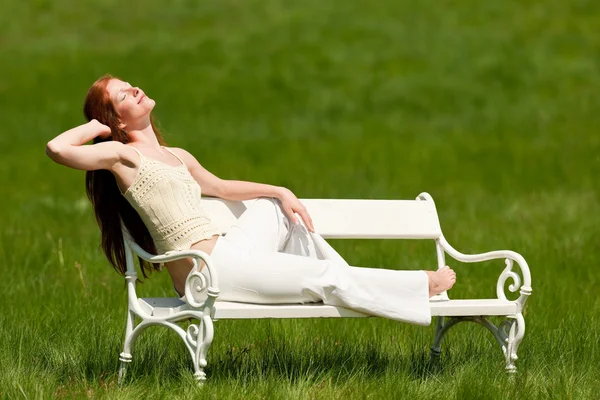 Femme aux cheveux roux profitant du soleil sur banc blanc au printemps — Photo