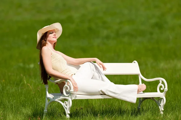 草原で白いベンチに座っている赤い髪の女性浅い被写し界深度 — ストック写真