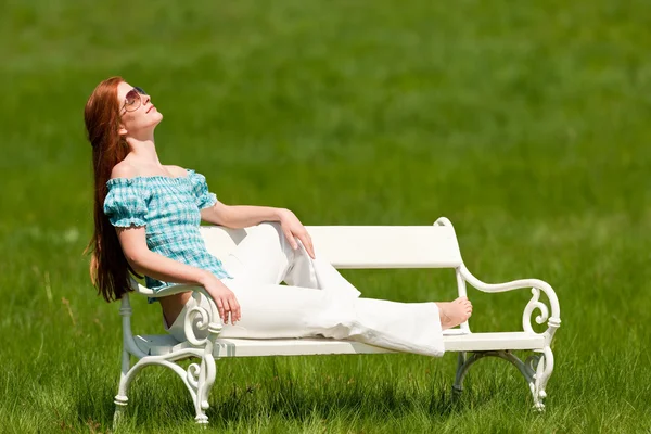 Czerwone włosy kobieta korzystających słońce na białym ławce na wiosnę — Zdjęcie stockowe