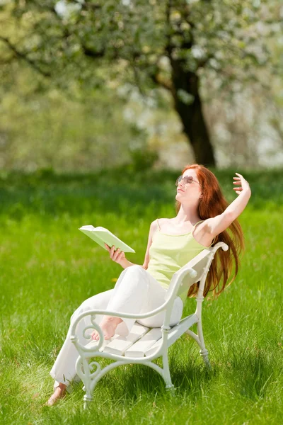 緑の牧草地 浅い被写し界深度で白いベンチに座って赤髪の女性 — ストック写真