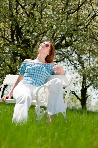 赤い髪の女性 草原で白いベンチに春の日差しを楽しんでいます 浅い被写し界深度 — ストック写真