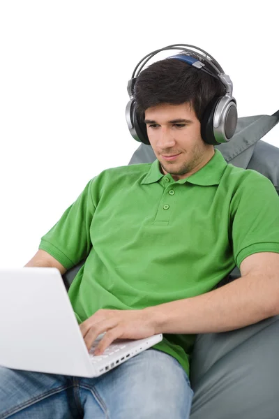 Dizüstü bilgisayar ve kulaklık oturan genç adam — Stok fotoğraf