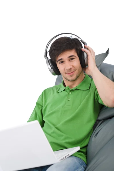 便携式电脑和耳机坐在白色背景上的豆袋上的年轻人 — 图库照片