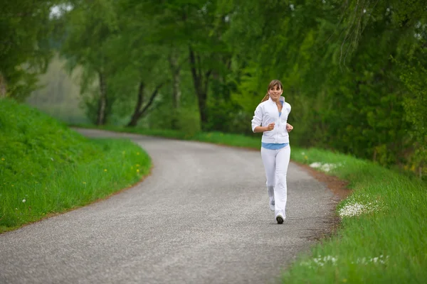 ジョギング 自然の中で道路上で実行されているスポーツの女性は イヤホンで音楽を聴く — ストック写真