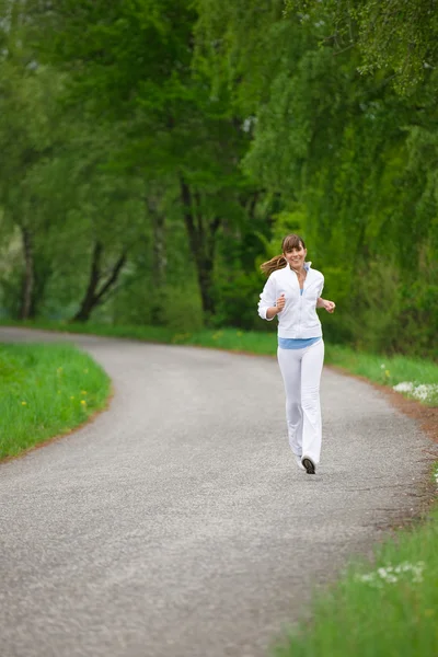 ジョギング 自然の中で道路上で実行されているスポーツの女性は イヤホンで音楽を聴く — ストック写真