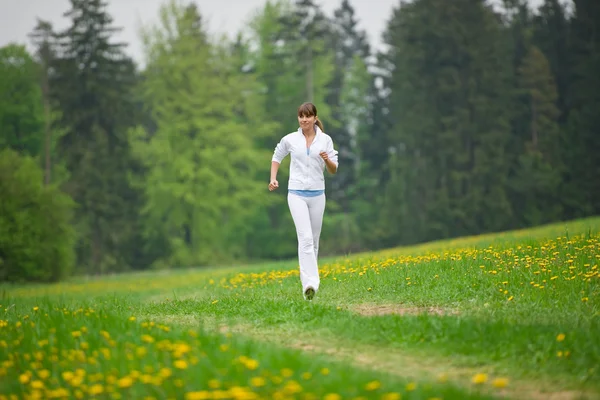 Біг спортивна жінка біжить в парку з кульбабою — стокове фото