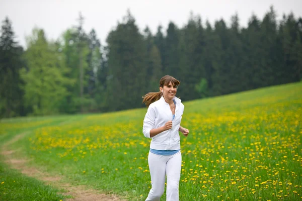 ジョギング 陽気なタンポポ 公園で走っている女性はイヤホンで音楽を聴く — ストック写真