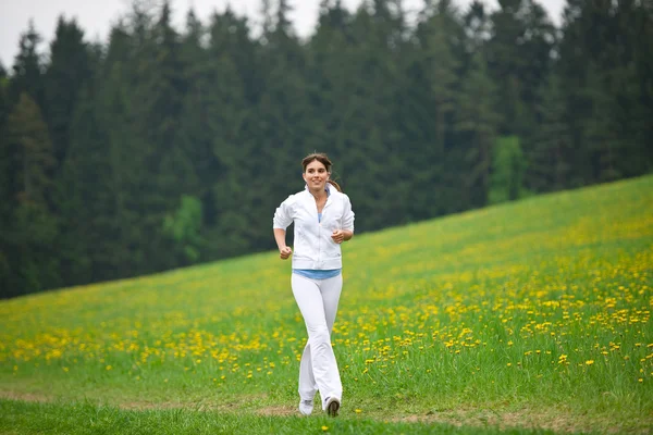 Joggen - sportliche Frau läuft im Park mit Löwenzahn — Stockfoto