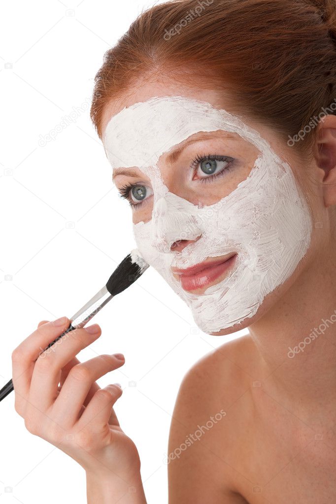 Young woman applying white facial mask using brush