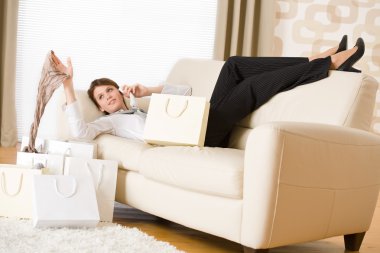 Young business woman lying down on sofa with luxury shopping bag, on the phone calling