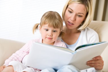 Mother with surprised little girl read book together in lounge clipart