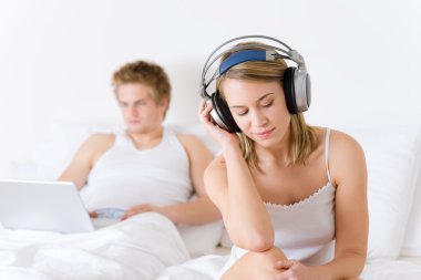 Genç çift yatakta müzik ve dizüstü bilgisayar ile rahatlayın.