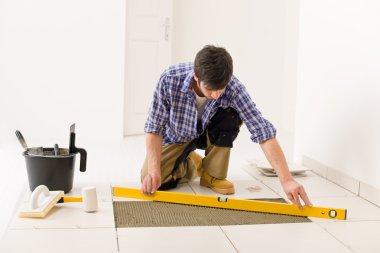 Home tile improvement - handyman with level laying down tile floor clipart