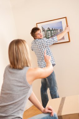 Moving house: Couple hanging picture on wall clipart