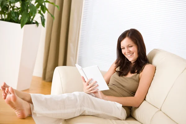 Νεαρή γυναίκα ευτυχισμένη διαβάσει βιβλίο στον καναπέ — Φωτογραφία Αρχείου