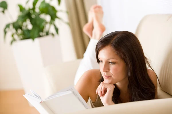 Ung kvinna läsa bok på soffa — Stockfoto