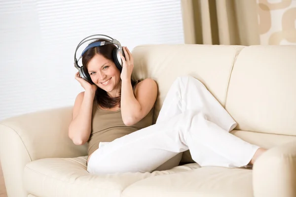 Mulher feliz com fones de ouvido no sofá no salão — Fotografia de Stock