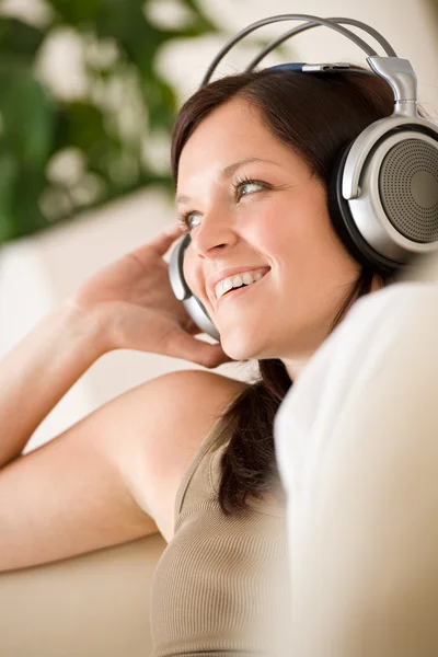 Donna sorridente con le cuffie ascolta musica in salotto — Foto Stock