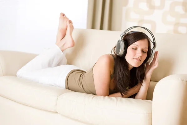 Glad kvinna med hörlurar på soffan i salongen — Stockfoto