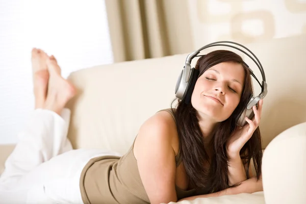 幸せな女ラウンジでは ソファに横たわってヘッドフォンで音楽を聴く — ストック写真