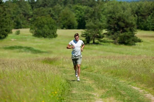 Giovane uomo con le cuffie che fa jogging in un prato — Foto Stock