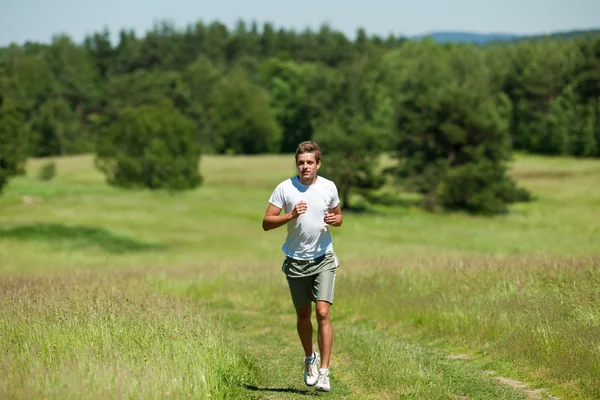 Junger Mann mit Kopfhörern joggt auf einer Wiese — Stockfoto