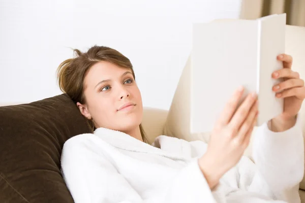 Młoda kobieta, poczytać książkę na kanapie na sobie szlafrok — Zdjęcie stockowe