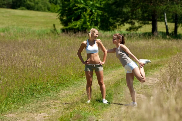 Dos mujeres jóvenes ejercitándose en un prado — Foto de Stock