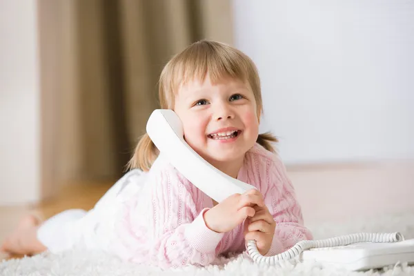 Usměvavá holčička vleže na koberci s telefonem — Stock fotografie