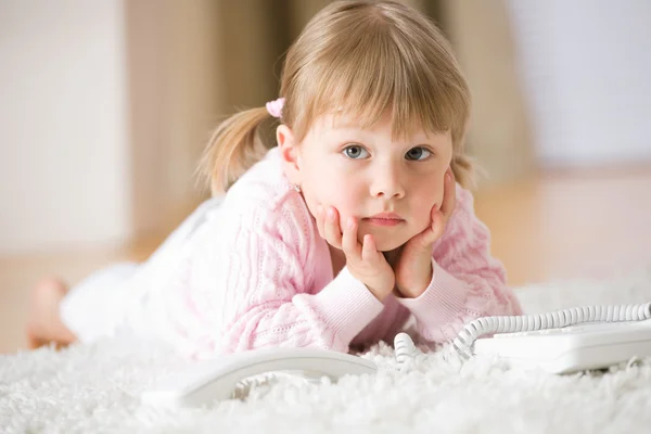 Little girl with telephone lying down on carpet — Stock Photo, Image