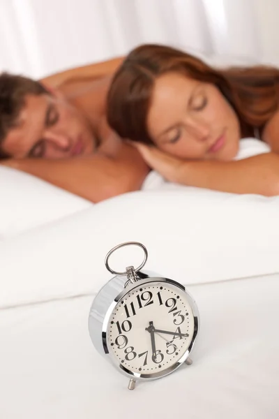 躺在白色的年轻夫妇上床闹钟 — 图库照片