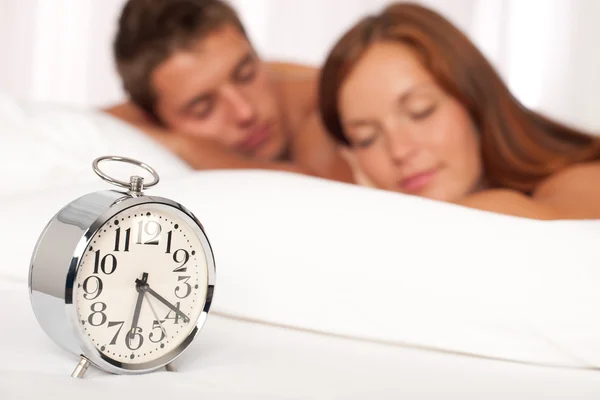 躺在白色的年轻夫妇上床银闹钟 — 图库照片