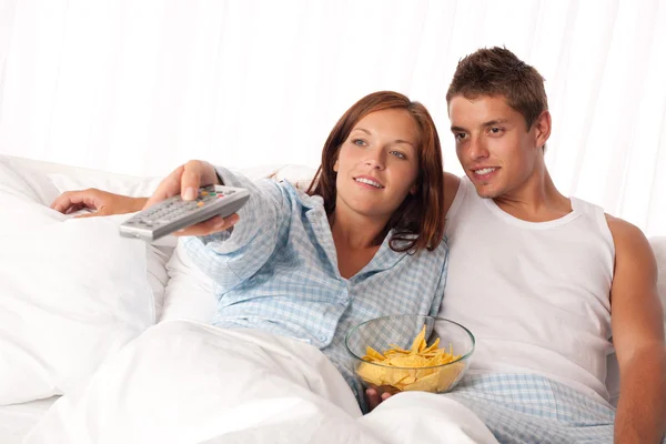 年轻女子和男子躺在床上看电视和吃薯片 — 图库照片