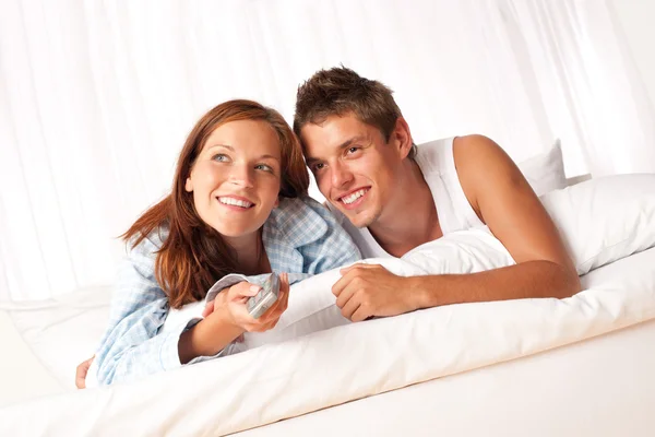 年轻的男人和女人躺在白色休息室看电视在一起 — 图库照片