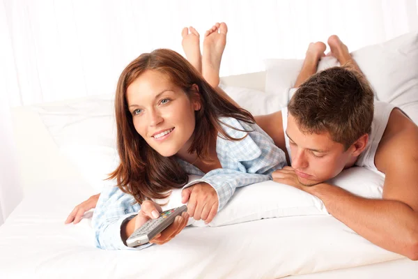 年轻的男人和女人躺在白色休息室看电视在一起 — 图库照片