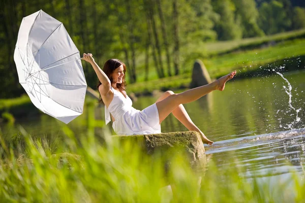 Счастливая романтичная женщина, сидящая у озера, брызгает водой — стоковое фото