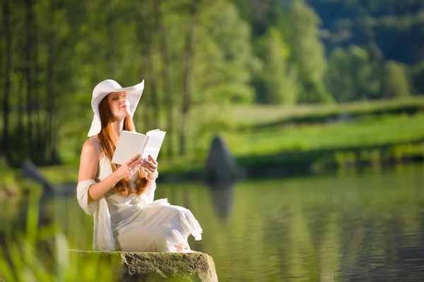 長い赤髪のロマンチックな女性の本と湖でリラックスします。 — ストック写真