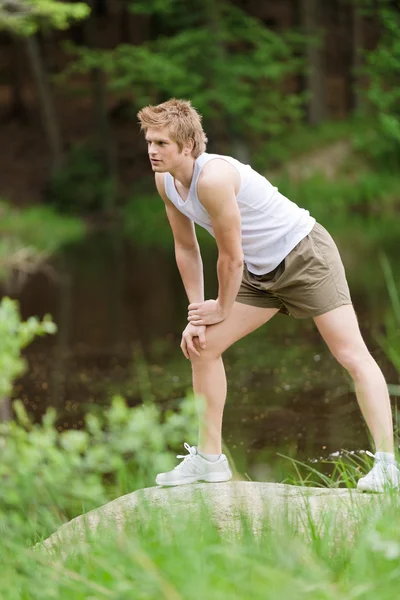 自然石の上に湖のそばに立ってのトレーニング後のストレッチ陽気な男 — ストック写真