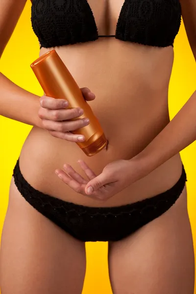 在黄色背景上穿黑色比基尼和一瓶防晒霜的女性身体的一部分 — 图库照片