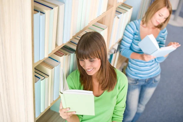 学生在图书馆 两个幸福的女人读的书从书架上 — 图库照片