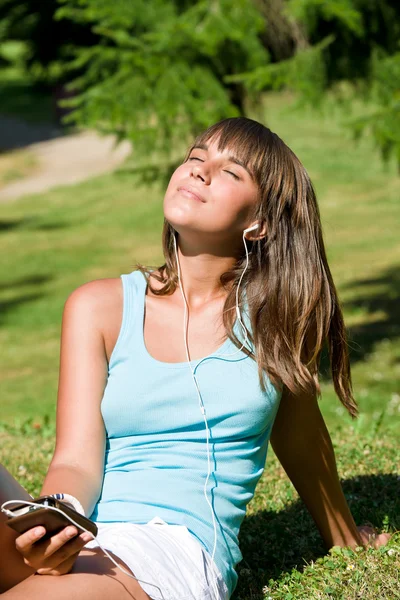 Jonge vrouw luisteren naar muziek in park — Stockfoto