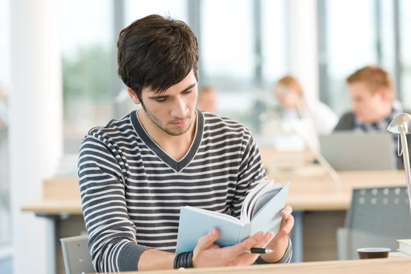 Ung manlig student läsa bok i klassrummet — Stockfoto