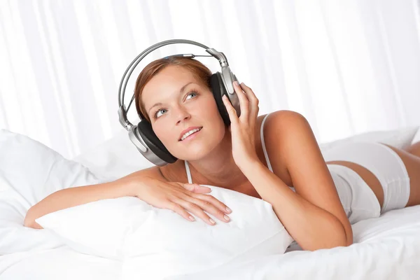 年轻女子在用耳机听音乐在卧室白色 — 图库照片
