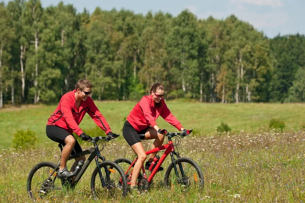 Młoda para jazda rower górski w wiosna łąka — Zdjęcie stockowe