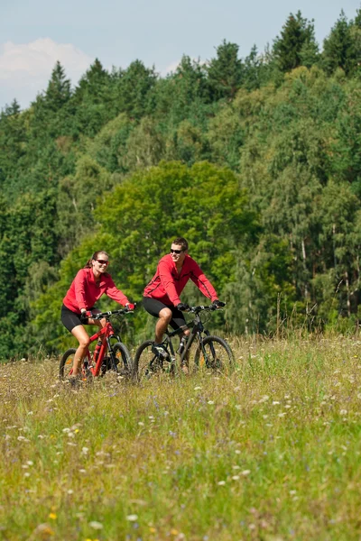 Jovem casal andar de bicicleta de montanha no prado da primavera — Fotografia de Stock
