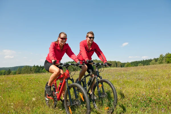 Jovem casal andar de bicicleta de montanha no prado da primavera — Fotografia de Stock